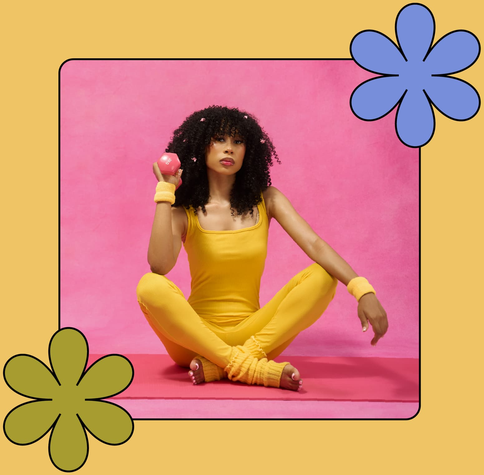 woman in the the diva wig with pink clips in her hair sitting crossed legged in yellow outfit holding a dumbbell on a pink yoga mat 