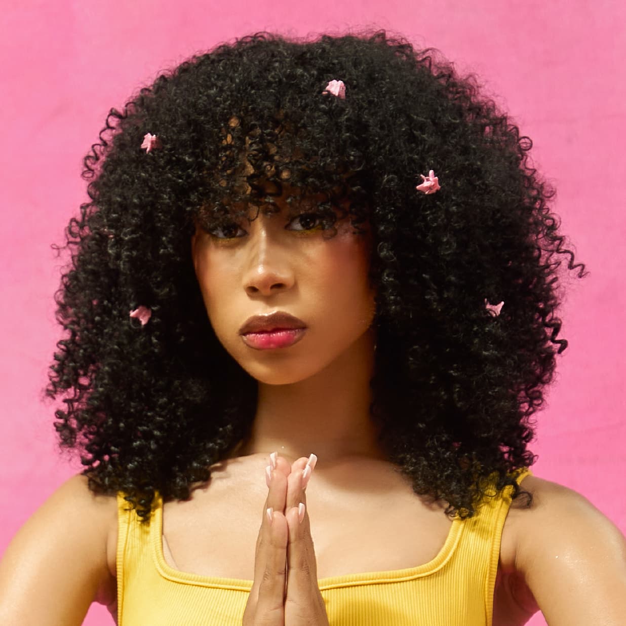 Woman wearing the afro-curly and voluminous DIVA wig with pink hair accessories against a pink background