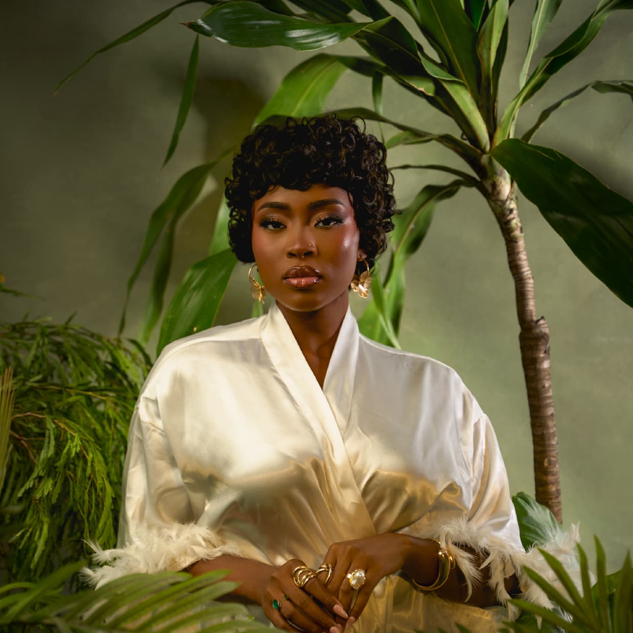 Woman in the Muse pixie wig wearing a white satin robe surrounded by green plants