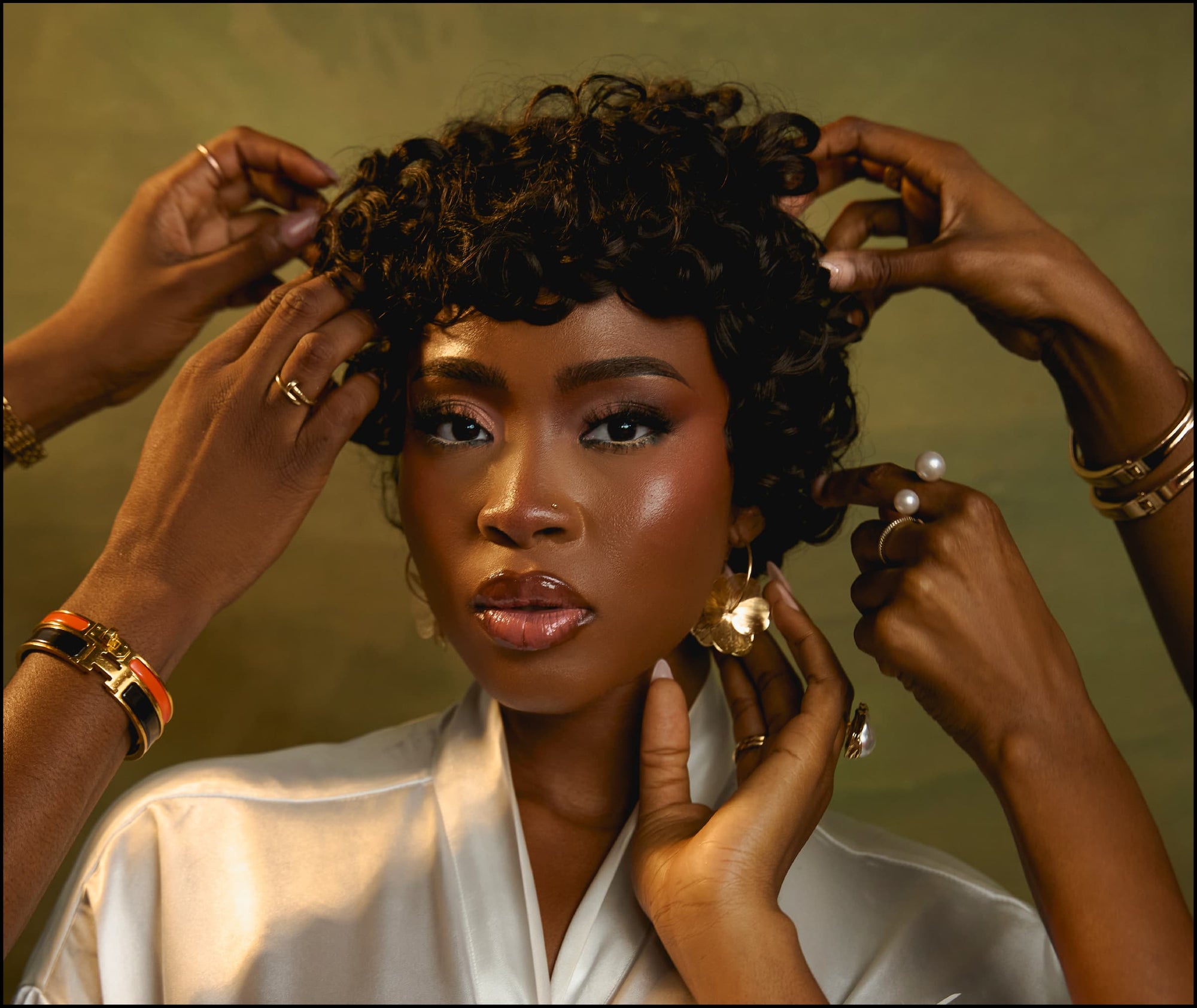 The Muse staring at the camera while four hands from off screen adjust her hair 